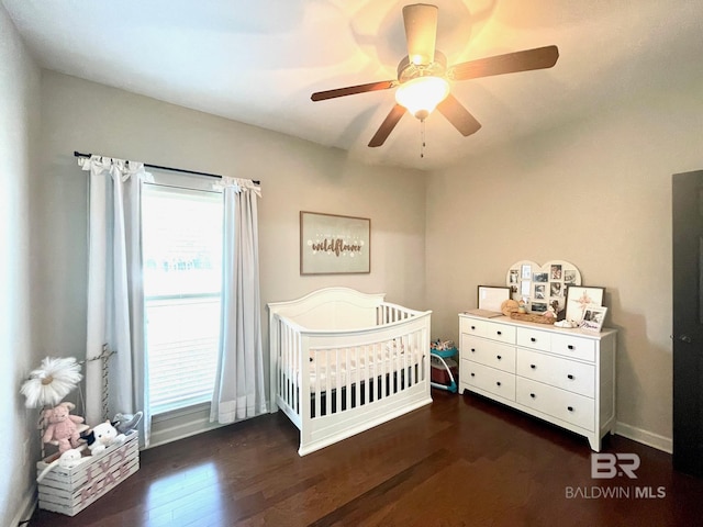 bedroom featuring a ceiling fan, a nursery area, wood finished floors, and baseboards