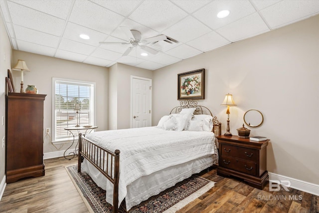 bedroom with dark wood-type flooring, a paneled ceiling, and ceiling fan