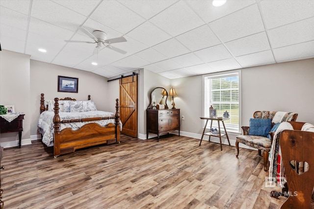 bedroom with a drop ceiling, hardwood / wood-style flooring, a barn door, and ceiling fan