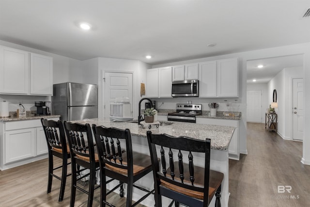 32299 Terranova Loop, Lillian, AL 36549 - kitchen featuring stainless steel appliances, a sink, wood finished floors, a kitchen bar, and white cabinetry