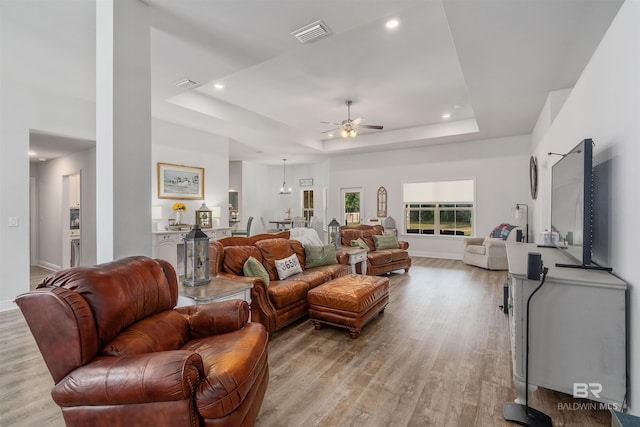 living room featuring ceiling fan, light wood-type flooring, and a raised ceiling