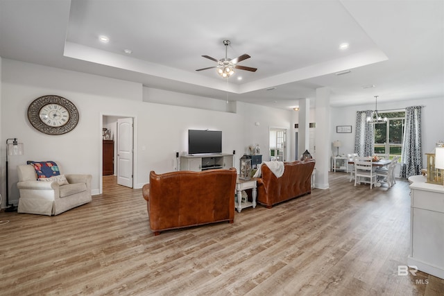 living room featuring ceiling fan with notable chandelier, a tray ceiling, and light wood-type flooring