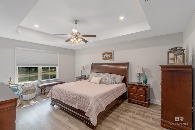 bedroom with light hardwood / wood-style flooring, a tray ceiling, and ceiling fan