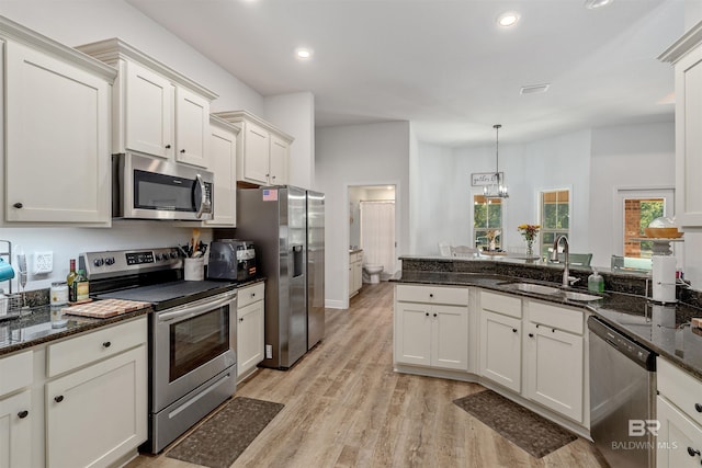 kitchen with hanging light fixtures, dark stone countertops, sink, appliances with stainless steel finishes, and light hardwood / wood-style floors