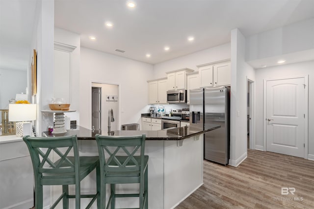 kitchen with stainless steel appliances, a kitchen bar, wood-type flooring, and kitchen peninsula