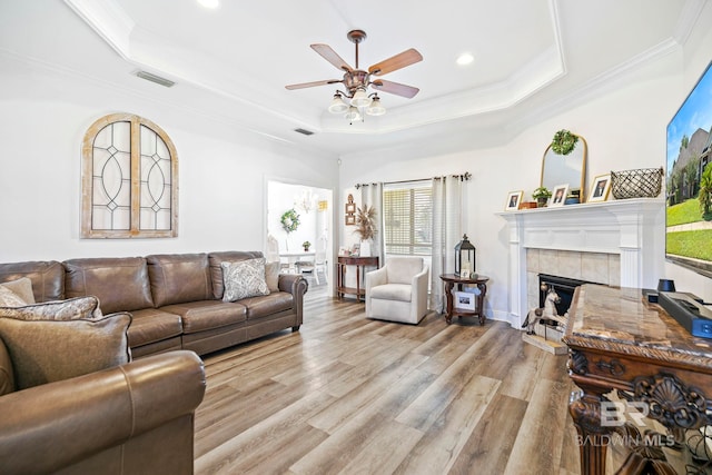 living room with light hardwood / wood-style floors, ornamental molding, a fireplace, a tray ceiling, and ceiling fan