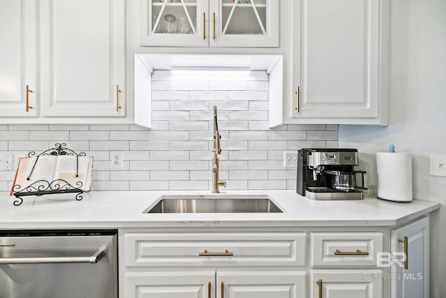 kitchen with stainless steel dishwasher, backsplash, white cabinets, light stone countertops, and sink