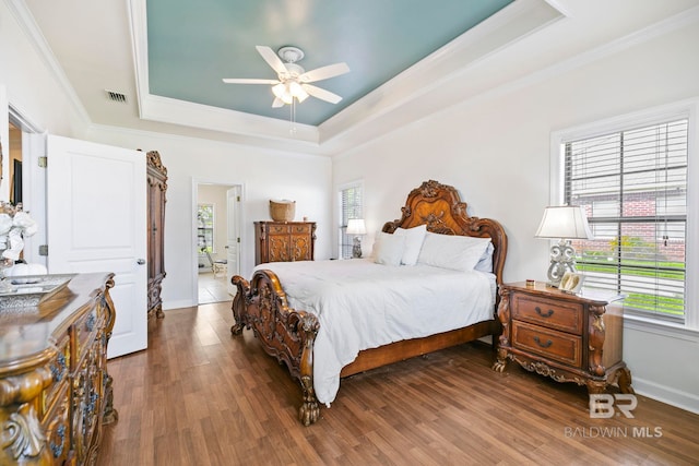 bedroom with multiple windows, a tray ceiling, and hardwood / wood-style floors