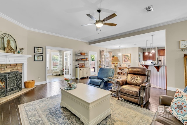 living room with ceiling fan, dark hardwood / wood-style floors, crown molding, and a stone fireplace