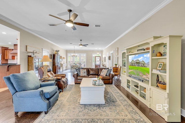 living room with ceiling fan with notable chandelier, wood-type flooring, built in features, and crown molding