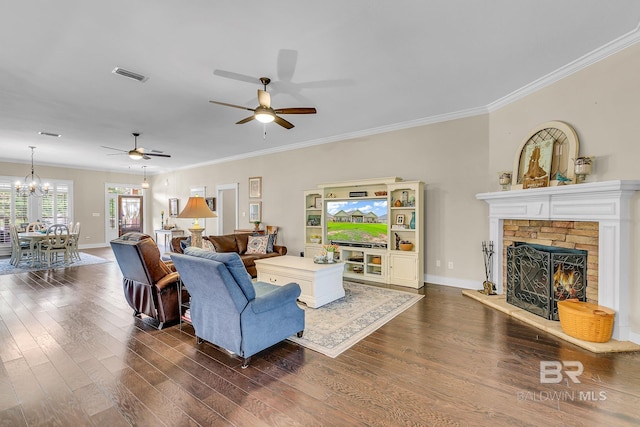 living room with ceiling fan with notable chandelier, dark wood-type flooring, ornamental molding, and a fireplace