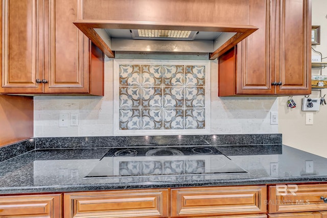 kitchen with decorative backsplash, black electric cooktop, dark stone counters, and custom range hood