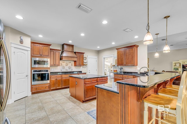 kitchen with kitchen peninsula, a kitchen breakfast bar, pendant lighting, premium range hood, and stainless steel appliances