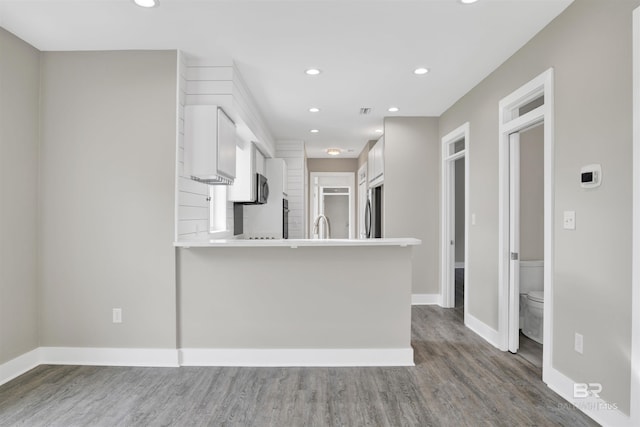 kitchen with hardwood / wood-style floors, kitchen peninsula, sink, white cabinets, and stainless steel fridge