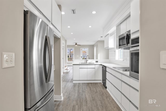 kitchen featuring kitchen peninsula, white cabinets, stainless steel appliances, and tasteful backsplash