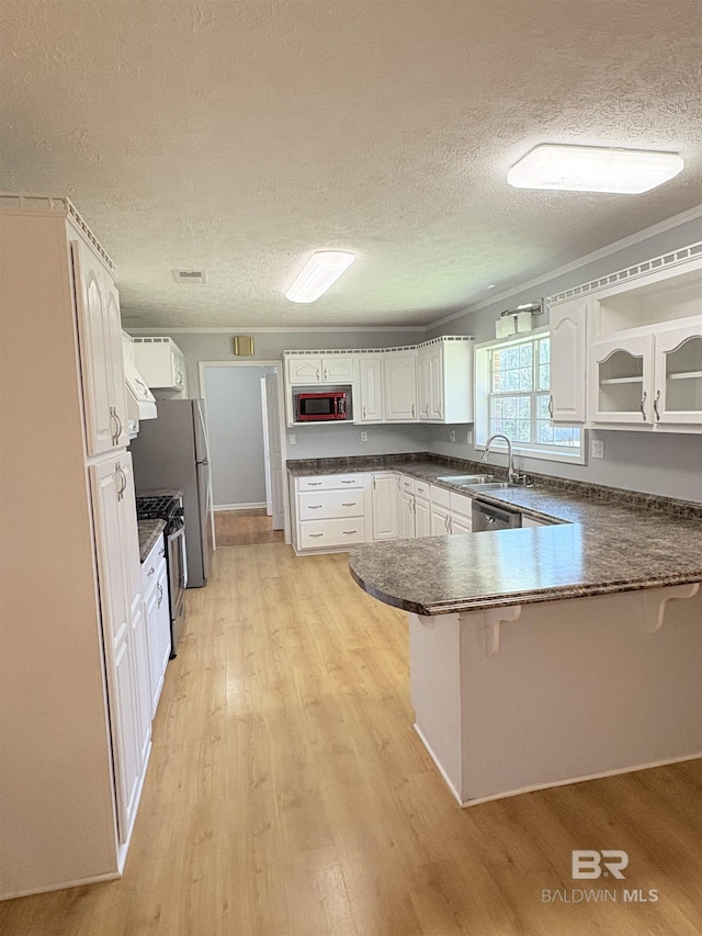 kitchen with appliances with stainless steel finishes, white cabinetry, sink, light hardwood / wood-style floors, and kitchen peninsula