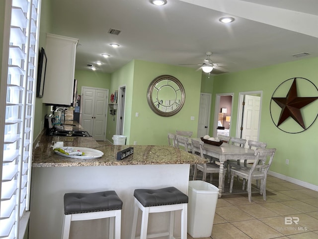 kitchen featuring kitchen peninsula, a breakfast bar, light tile patterned floors, white cabinets, and ceiling fan