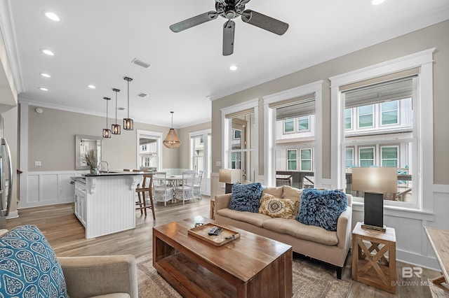 living area featuring a healthy amount of sunlight, light wood finished floors, ornamental molding, and a decorative wall