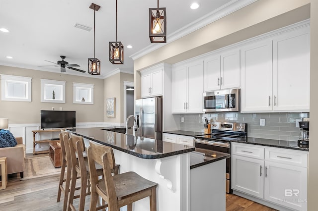 kitchen with decorative light fixtures, white cabinetry, open floor plan, appliances with stainless steel finishes, and a center island with sink