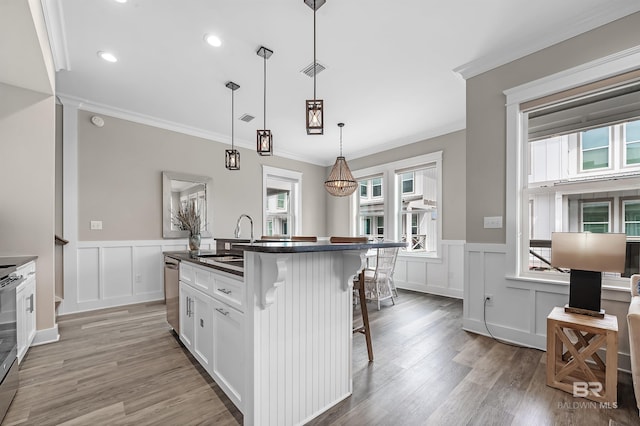 kitchen with white cabinets, hanging light fixtures, dark countertops, a kitchen bar, and a center island with sink