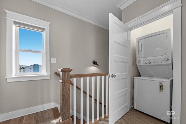 clothes washing area with laundry area, wood finished floors, baseboards, stacked washer and clothes dryer, and crown molding