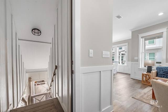 hallway with visible vents, a wainscoted wall, ornamental molding, wood finished floors, and an upstairs landing