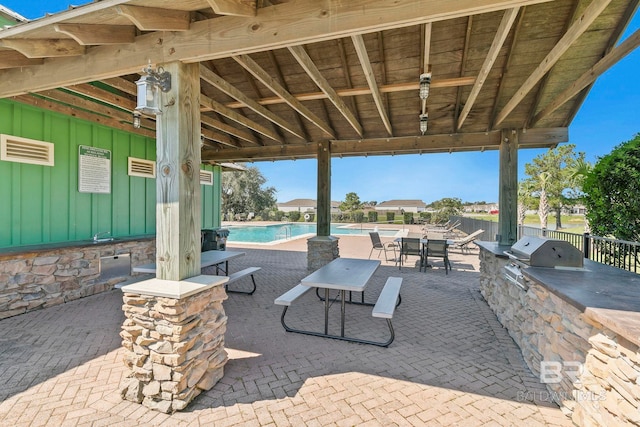 view of patio with exterior kitchen, grilling area, and a community pool