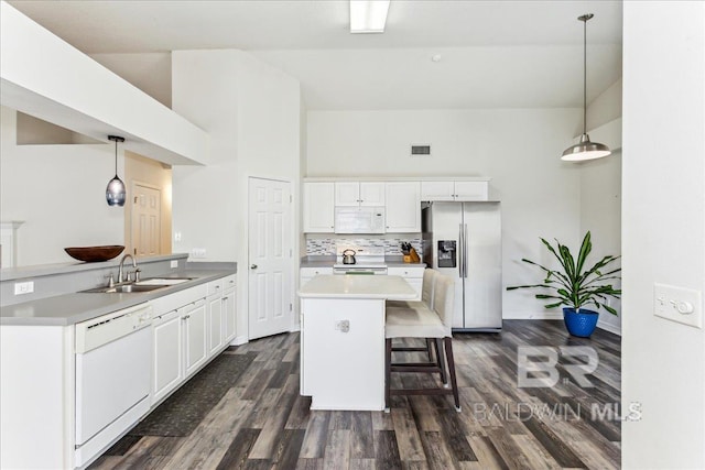 kitchen featuring dark wood finished floors, backsplash, white cabinets, a sink, and white appliances