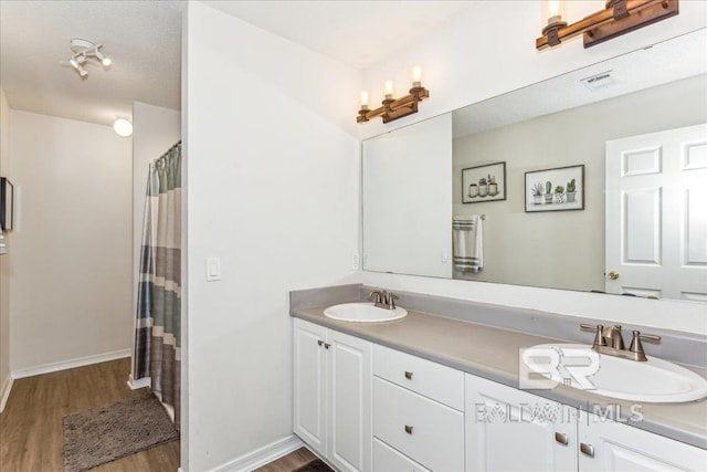 bathroom with double vanity, visible vents, a sink, and wood finished floors