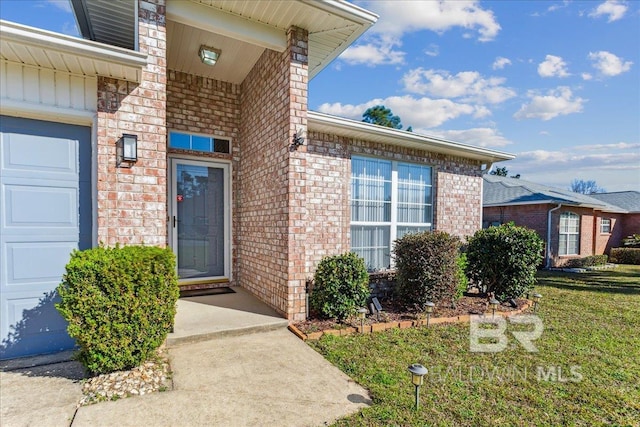 doorway to property with a yard, brick siding, and an attached garage