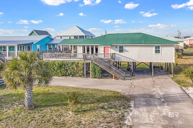 raised beach house with a porch, stairway, metal roof, a carport, and driveway