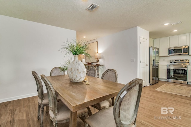 dining room with visible vents, baseboards, light wood-style flooring, a textured ceiling, and recessed lighting