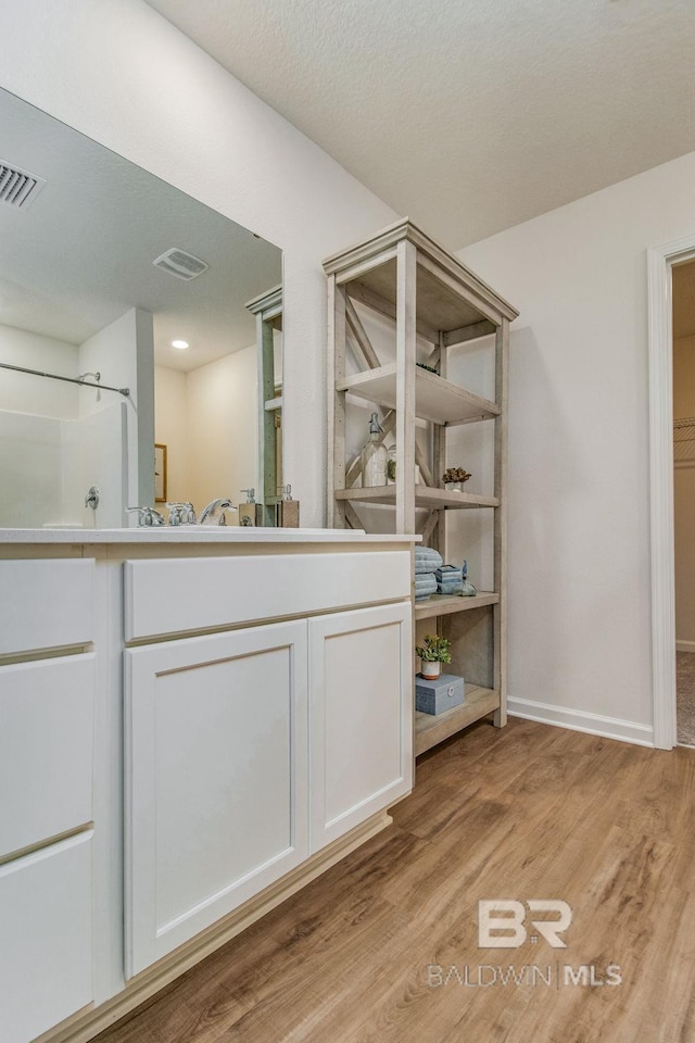 bathroom with visible vents, vanity, baseboards, and wood finished floors