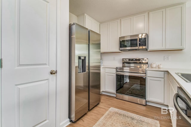 kitchen with light countertops, appliances with stainless steel finishes, light wood-style floors, white cabinetry, and a textured ceiling