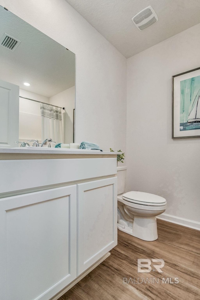 bathroom with visible vents, vanity, toilet, and wood finished floors