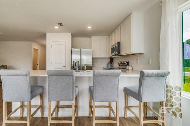 kitchen with appliances with stainless steel finishes, a breakfast bar area, a peninsula, light countertops, and white cabinetry