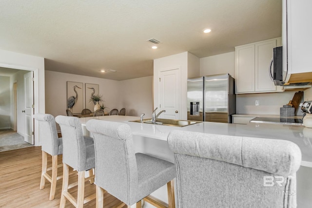 kitchen featuring stainless steel refrigerator with ice dispenser, visible vents, light countertops, white cabinetry, and a sink