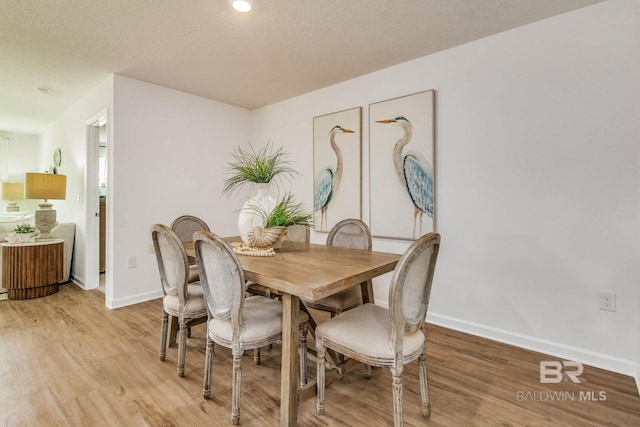 dining space with baseboards, a textured ceiling, and light wood-style floors