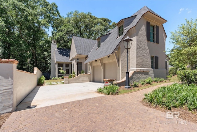 view of side of property with driveway, a garage, fence, a chimney, and stucco siding