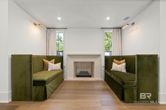 sitting room with healthy amount of natural light, wood finished floors, a fireplace with raised hearth, and recessed lighting