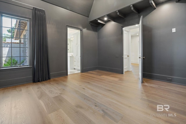unfurnished room featuring light wood-style flooring, plenty of natural light, baseboards, and lofted ceiling