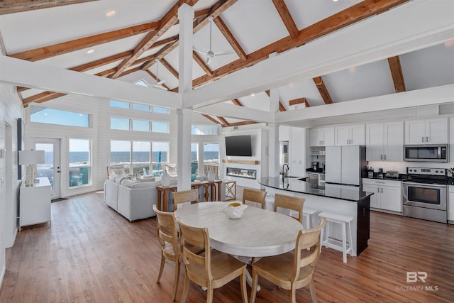 dining space with ceiling fan, beamed ceiling, sink, wood-type flooring, and high vaulted ceiling