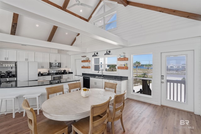 dining room with sink, light wood-type flooring, beam ceiling, and high vaulted ceiling