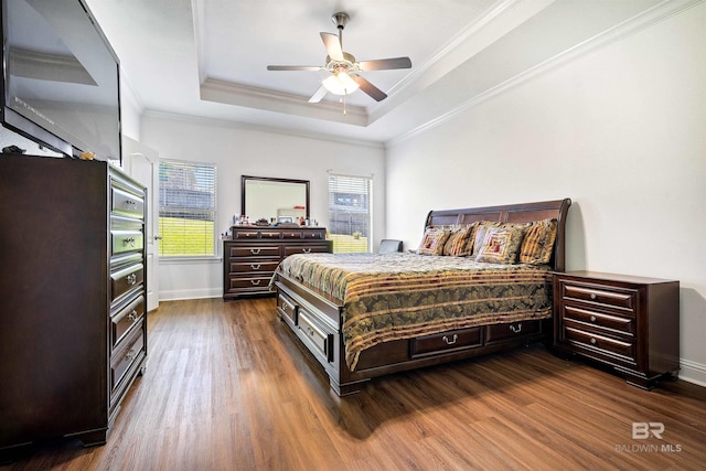 bedroom featuring dark wood-type flooring, ornamental molding, baseboards, a raised ceiling, and ceiling fan