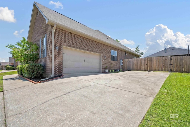 view of home's exterior with brick siding, a garage, fence, driveway, and roof with shingles