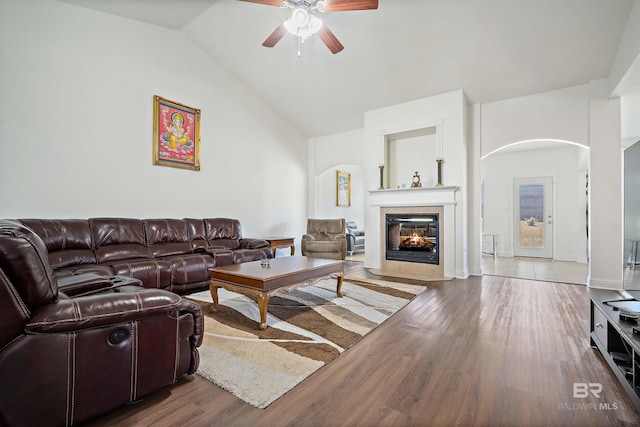 living room with arched walkways, a ceiling fan, a tile fireplace, wood finished floors, and high vaulted ceiling