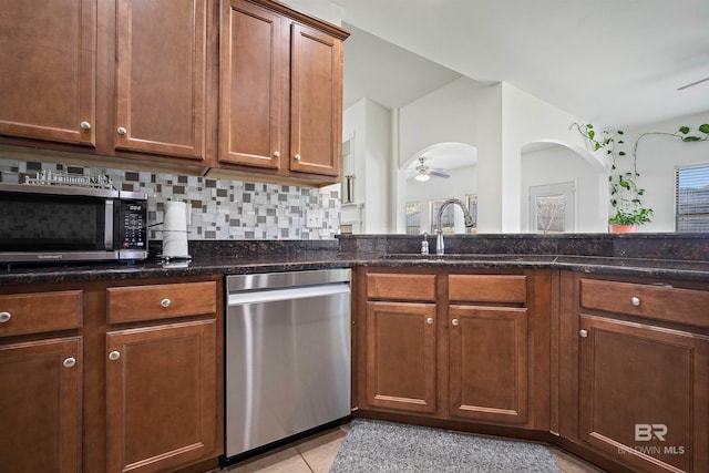 kitchen featuring stainless steel appliances, backsplash, dark stone countertops, light tile patterned floors, and a ceiling fan