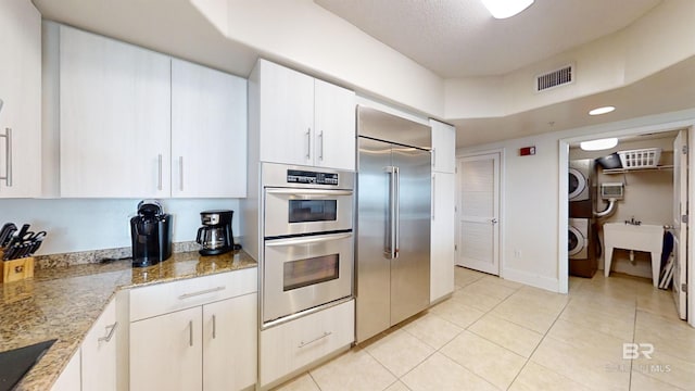 kitchen featuring light tile patterned floors, stacked washing maching and dryer, light stone counters, visible vents, and appliances with stainless steel finishes