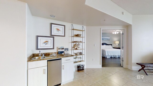 interior space with refrigerator, baseboards, a sink, light tile patterned flooring, and indoor wet bar