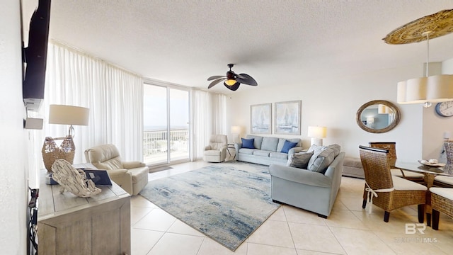 living area with a ceiling fan, light tile patterned flooring, a wall of windows, and a textured ceiling